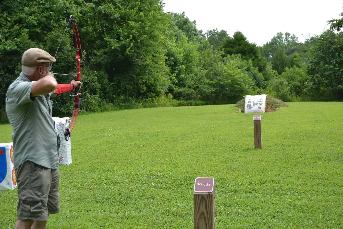 Archer drawing a recurve bow at an outdoor archery range with yardage markers