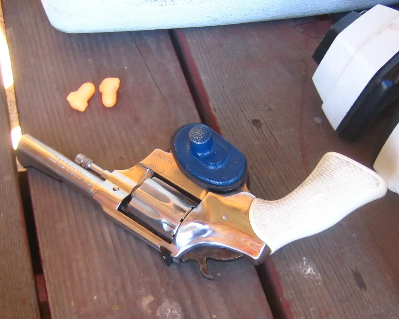 Revolver with a trigger lock beside foam earplugs and earmuffs on a range bench